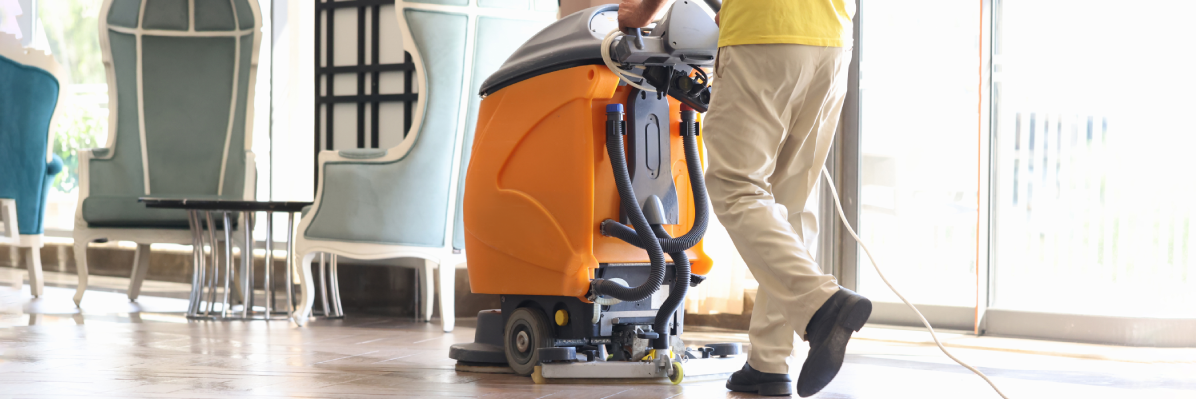 Photo of a person cleaning a floor with a yellow scrubber dryer