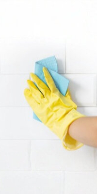 Hand wearing yellow rubber glove scrubbing tile grout