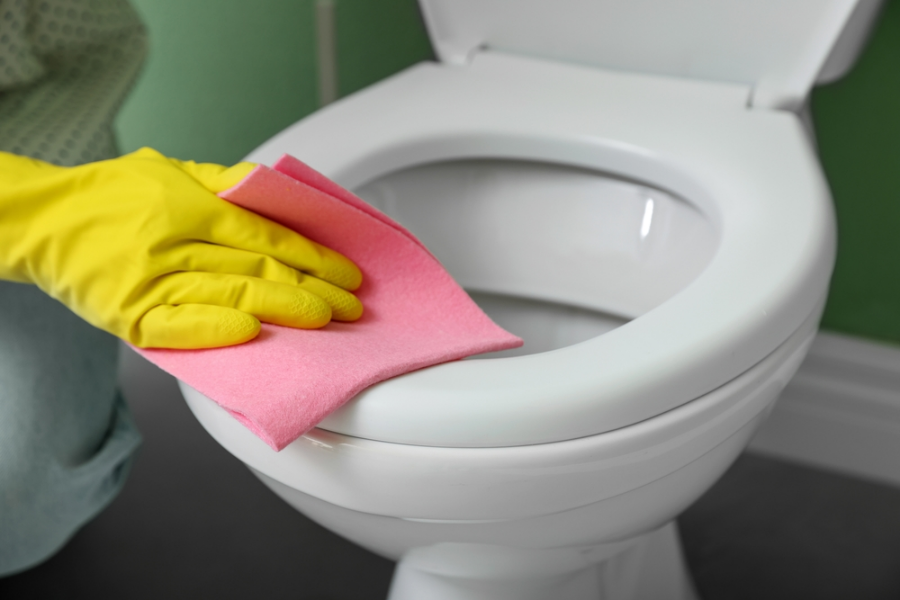 A person cleaning a toilet rim with a red cloth