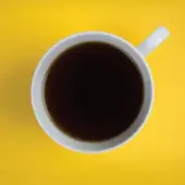Birds-eye view photo of a coffee cup on a yellow desk