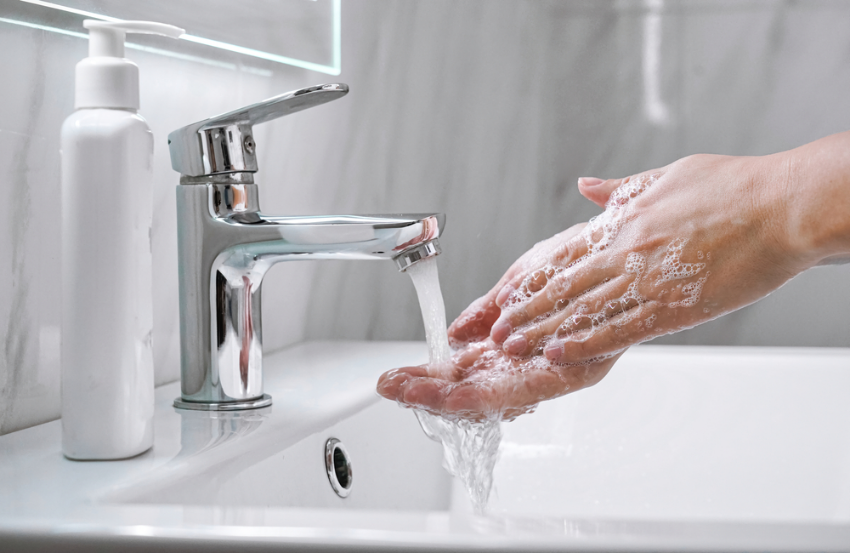 Hands being washed in modern sink with marble tiled walls