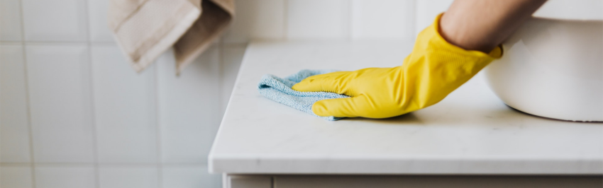 Person cleaning a marble bathroom worktop wearing yellow rubber gloves